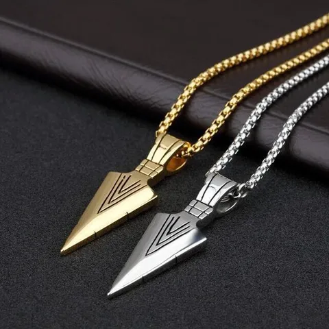 Two arrowhead-shaped pendants on gold and silver chains against a dark background