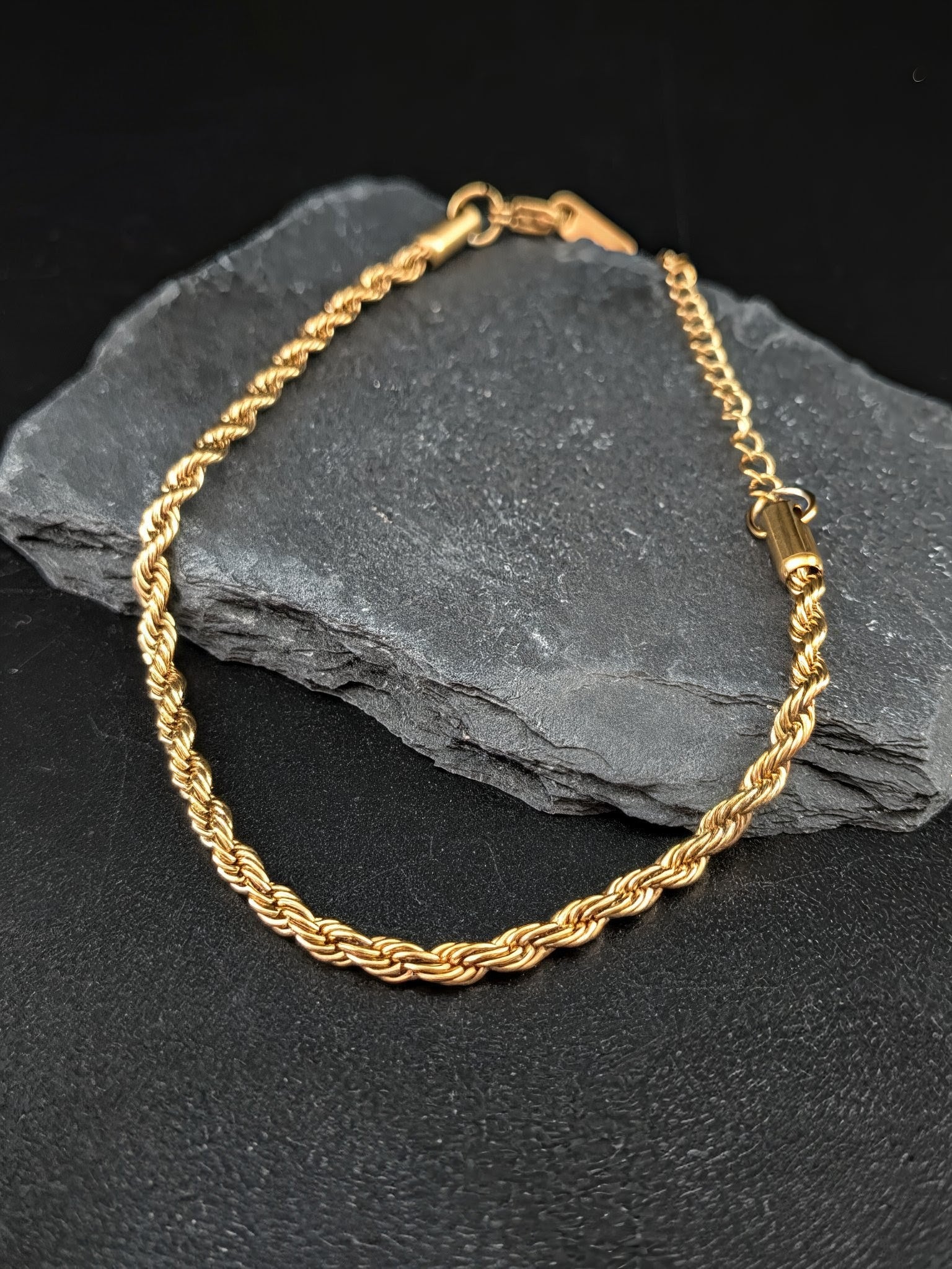 Gold rope chain bracelet on a dark stone surface