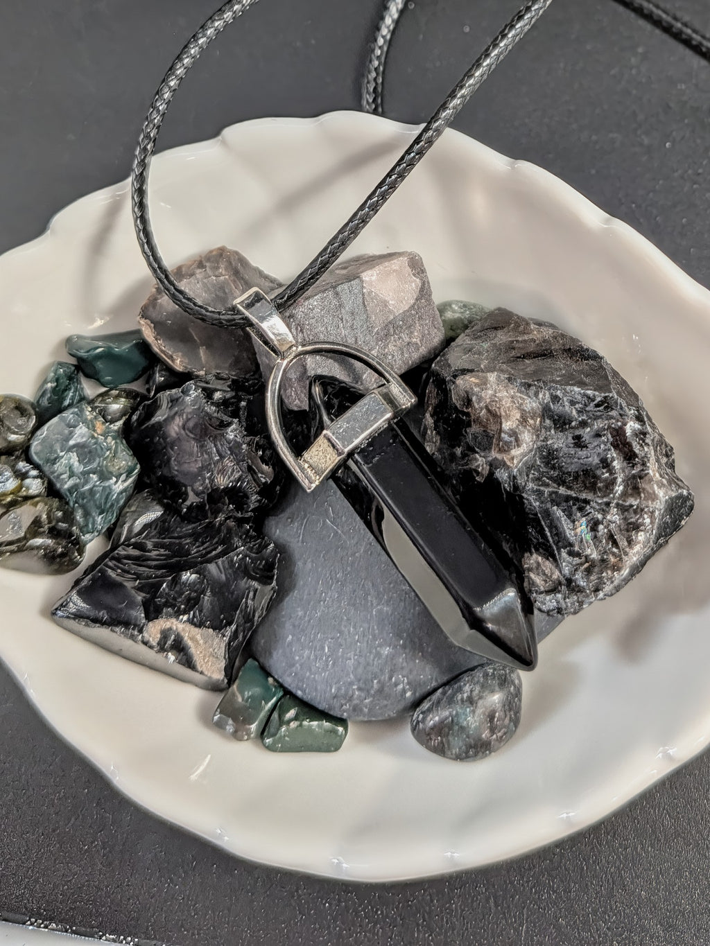 Necklace with a pendant on a white dish with dark stones