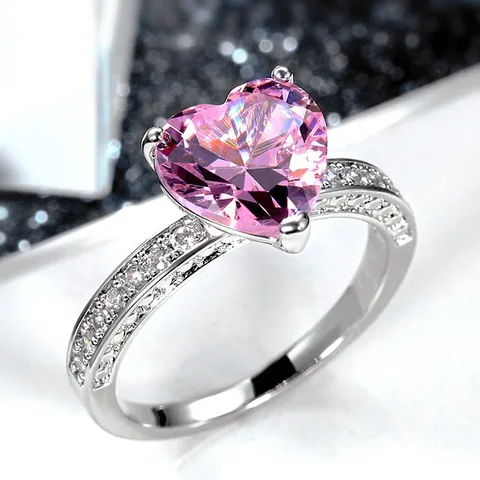 Heart-shaped pink gemstone ring with silver band on a white background