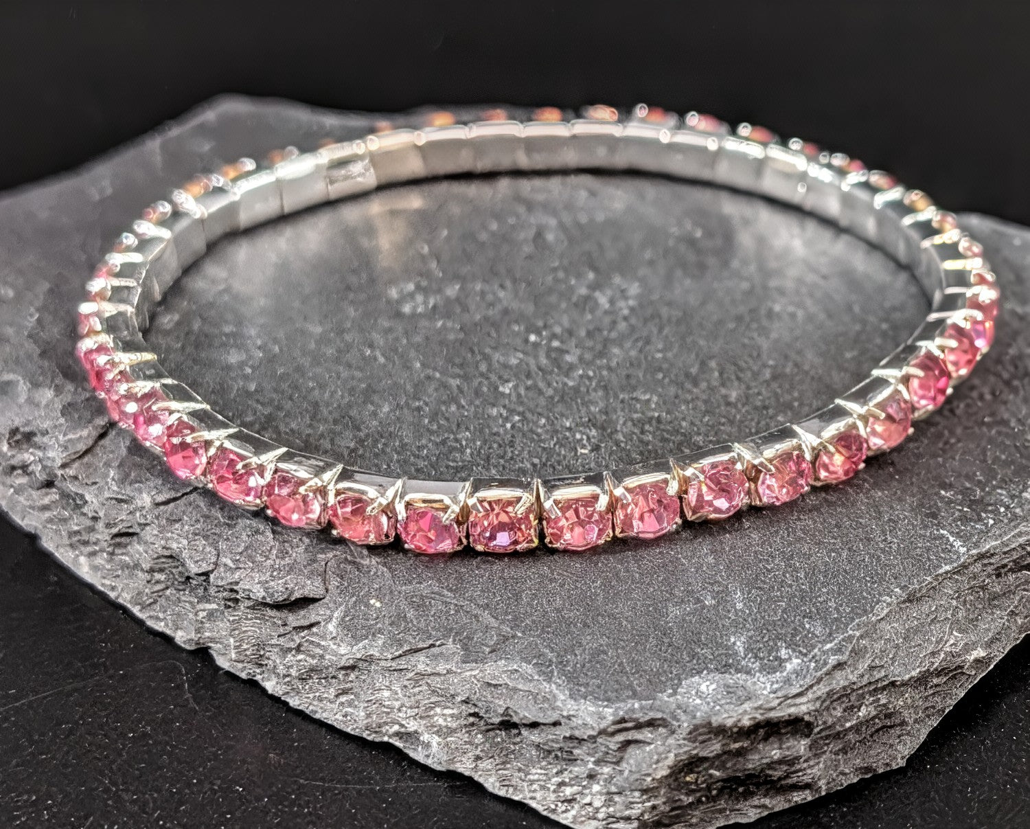 Silver bracelet with pink gemstones on a dark stone surface