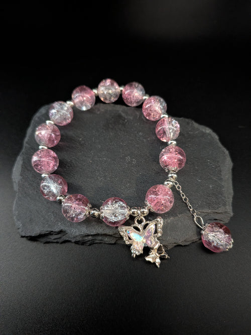 Bracelet with pink and clear beads and a butterfly charm on a dark surface