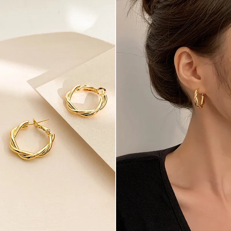 Gold hoop earrings on a beige surface and worn by a person.