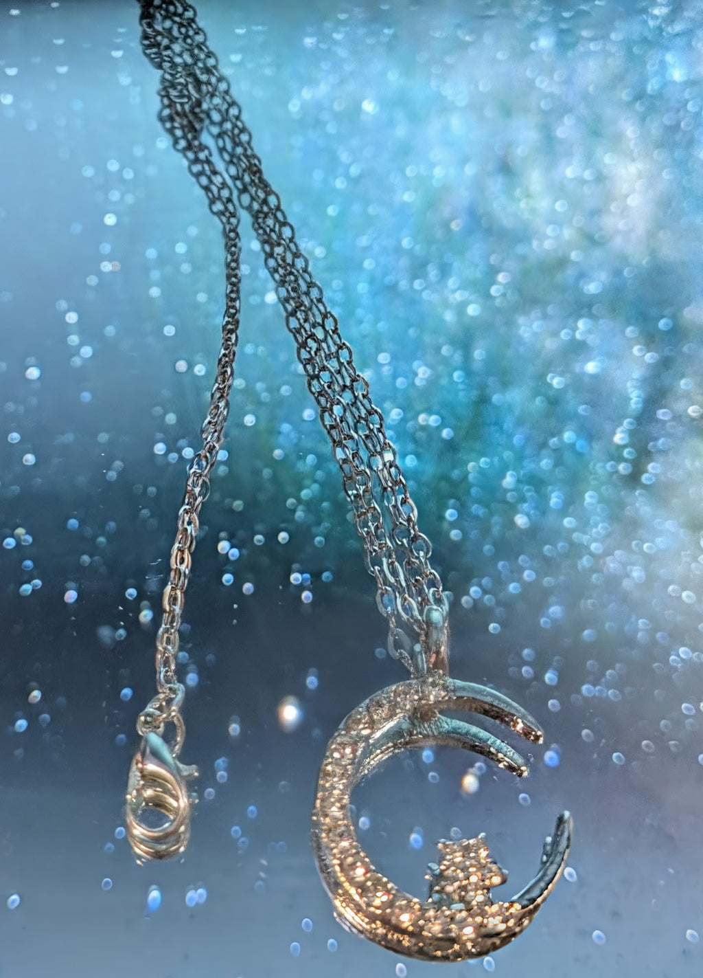 Silver necklace with a moon-shaped pendant against a sparkling blue background