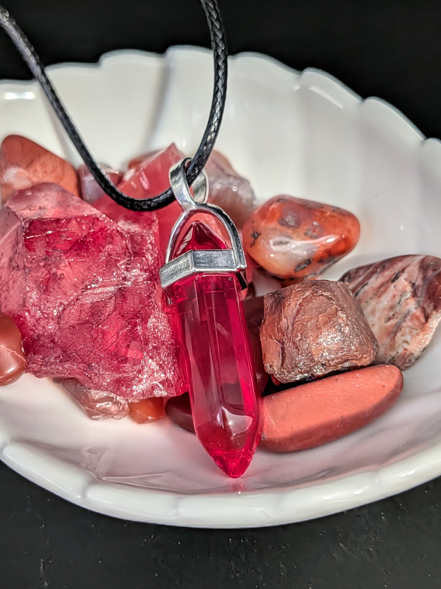 Red crystal pendant on a black cord with raw red crystals in a white bowl.
