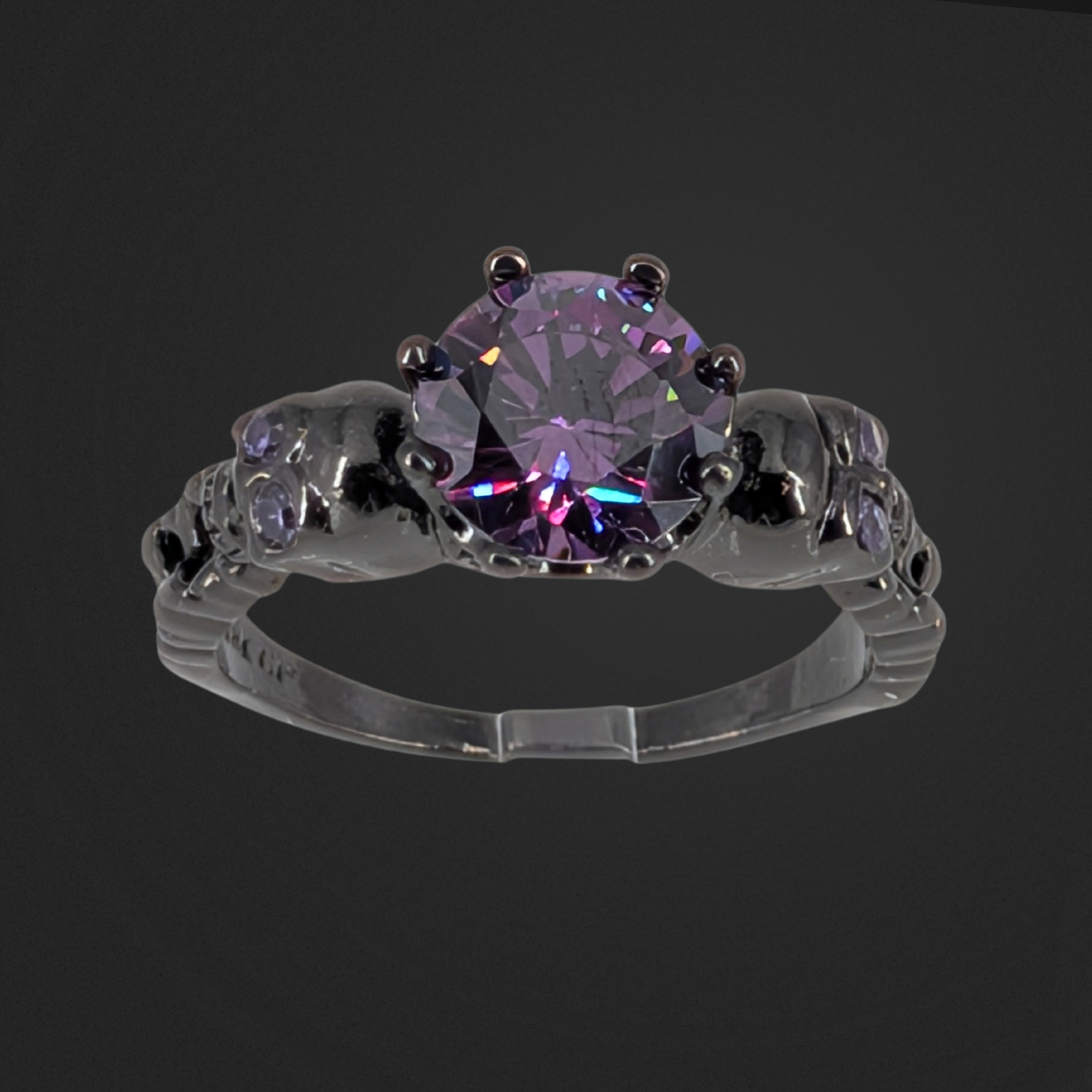 Gothic ring with a purple gemstone on a black background. Two skull on either side of gemstone.