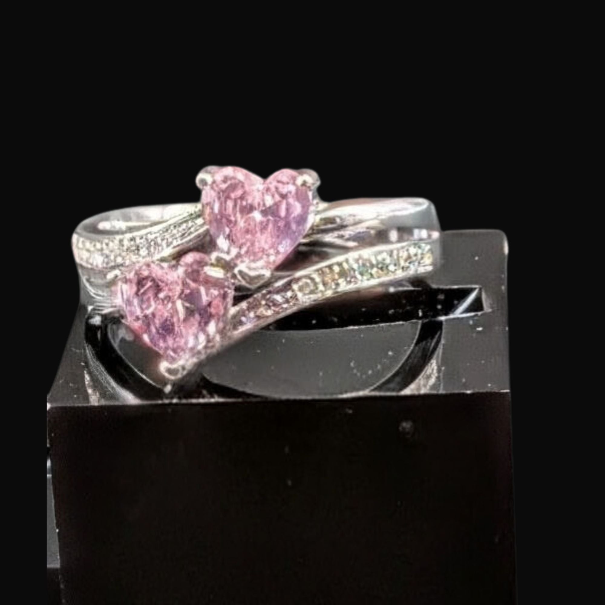 Silver ring with pink heart-shaped gemstones on a black stand