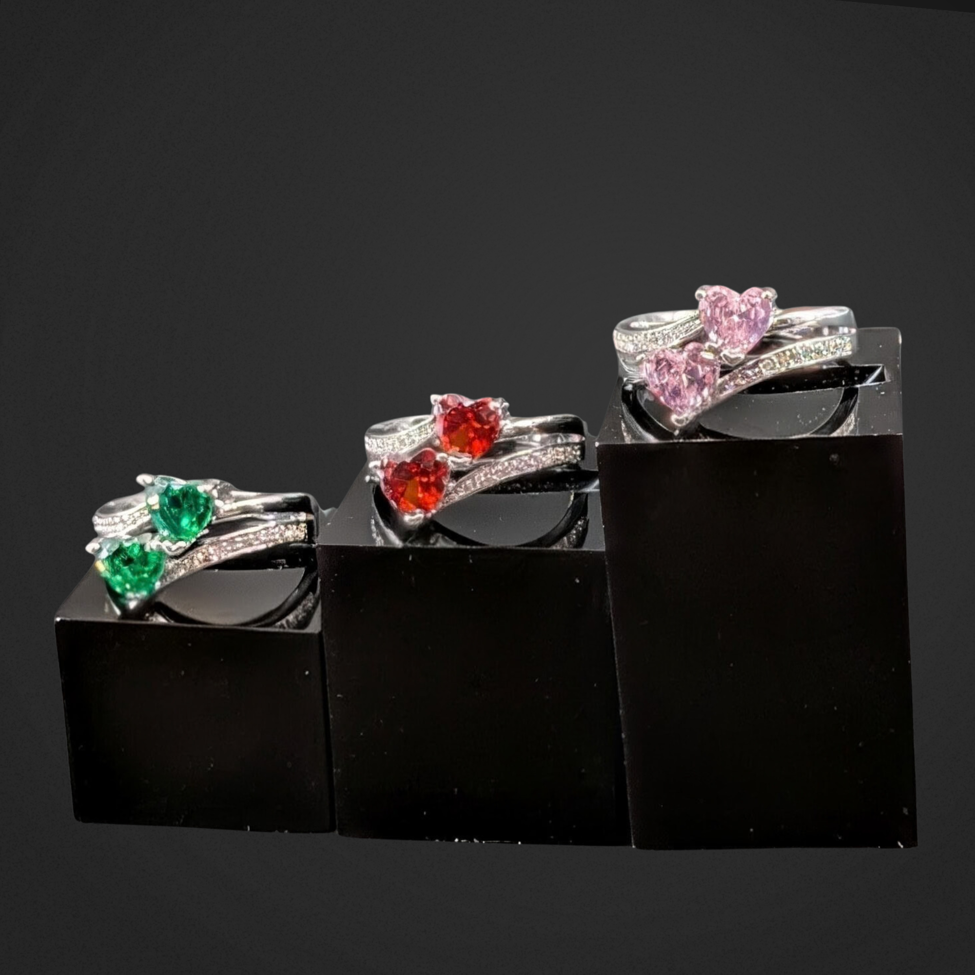 Three heart-shaped gemstone rings on a black stand against a dark background