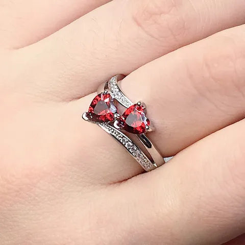 Close-up of a hand wearing two heart-shaped gemstone rings.
