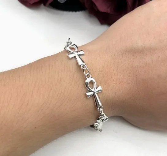 Silver bracelet with ankh symbols on a wrist against a white background