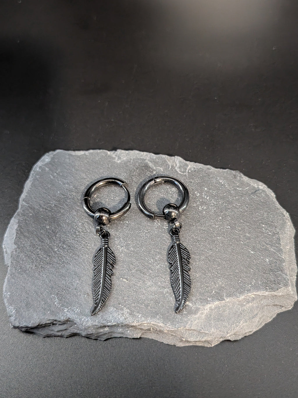 Pair of silver feather earrings on a gray stone surface with a dark background