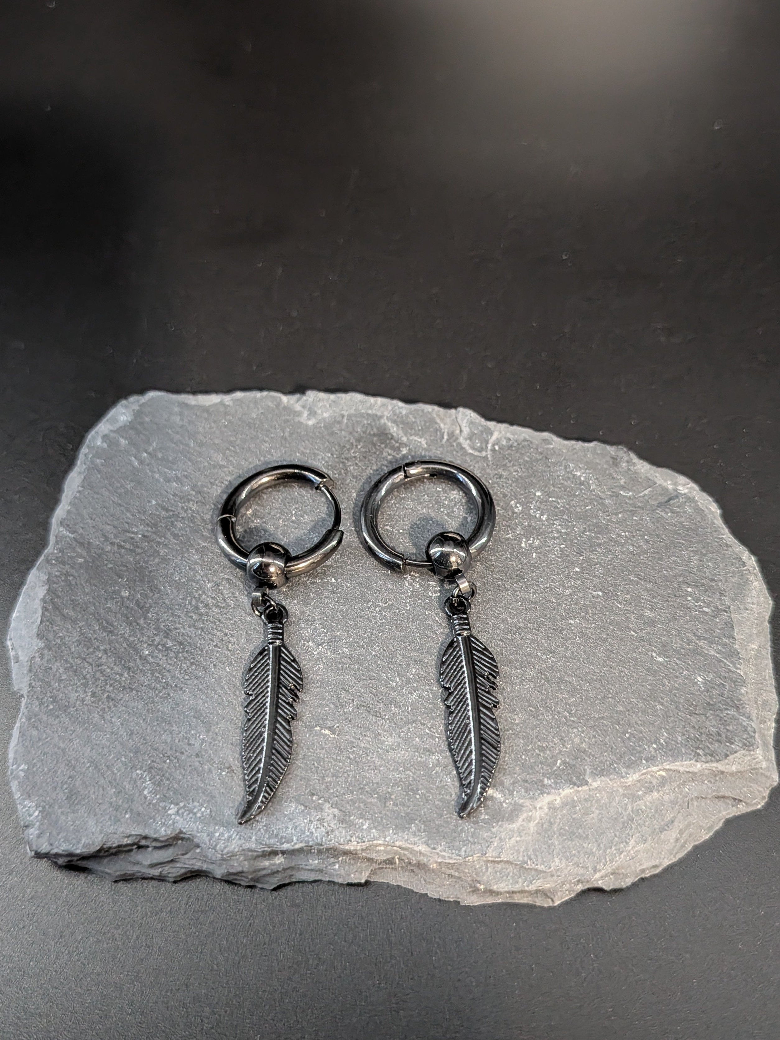 Pair of silver feather earrings on a gray stone surface with a dark background