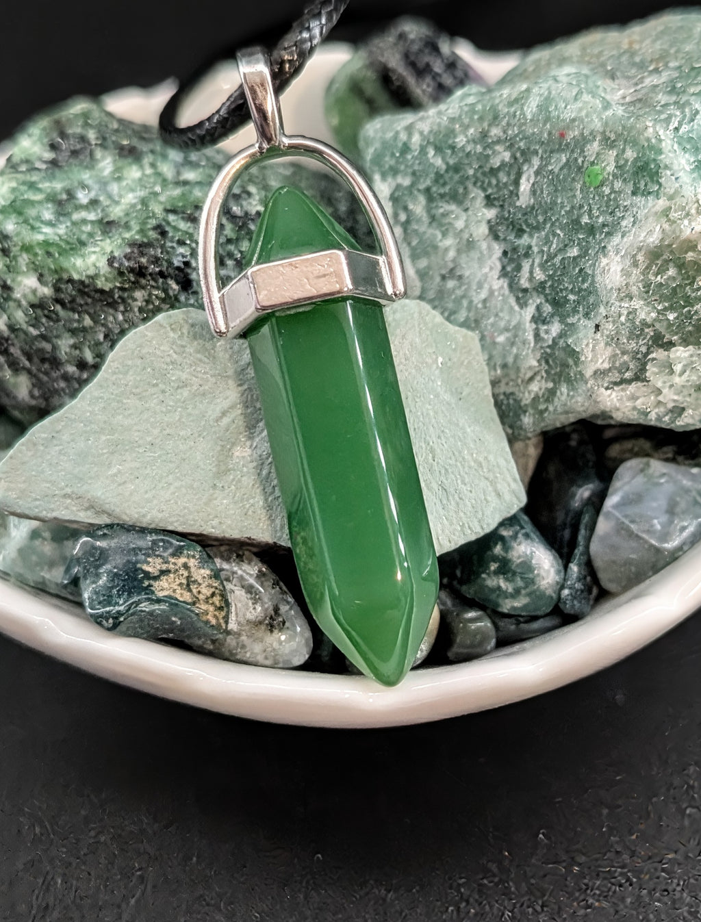 Green crystal pendant on a silver chain against a background of green stones.
