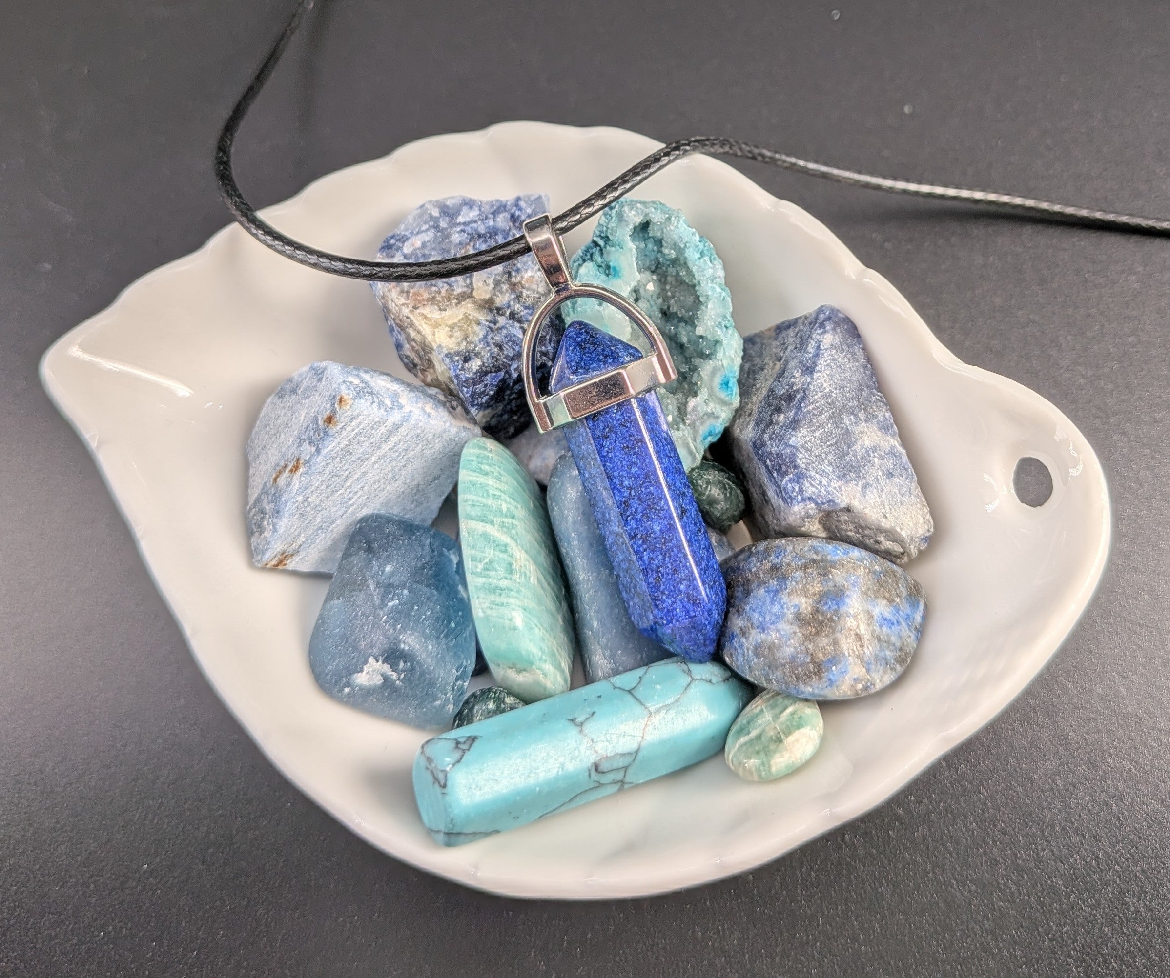 Crystal necklace with blue and green stones on a white dish against a gray background