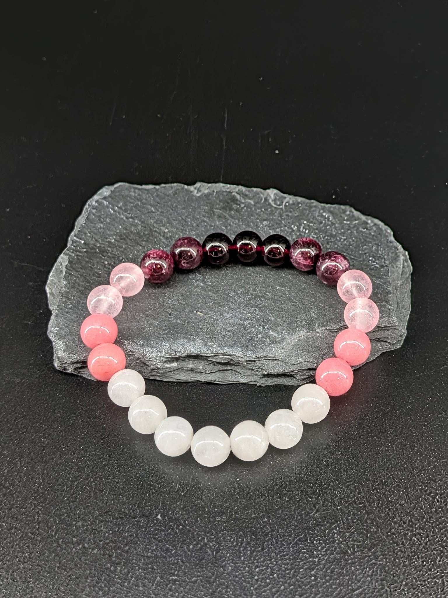 Beaded bracelets on a dark surface with a gray stone