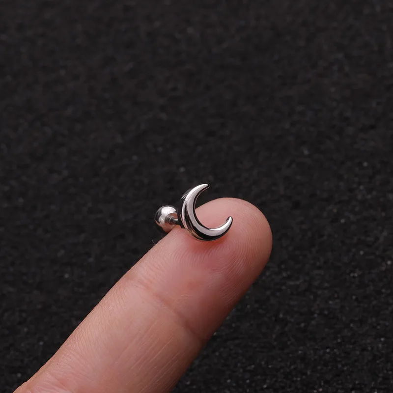 Silver moon-shaped earring on a finger against a black background