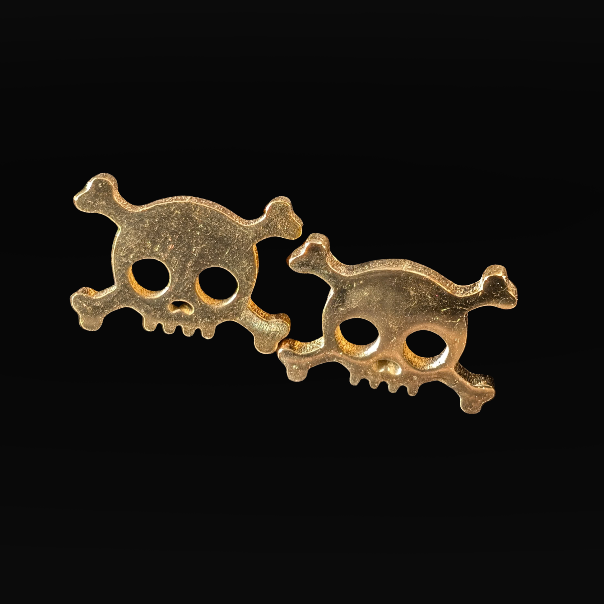 Two gold skull and crossbones earrings on a black background
