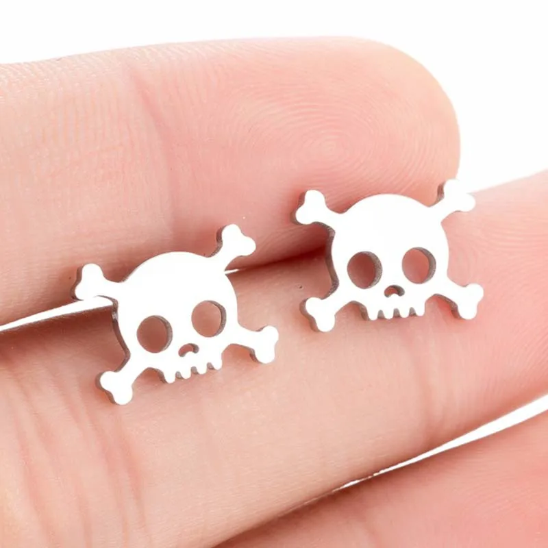 Skull-shaped earrings held between fingers on a light skin background
