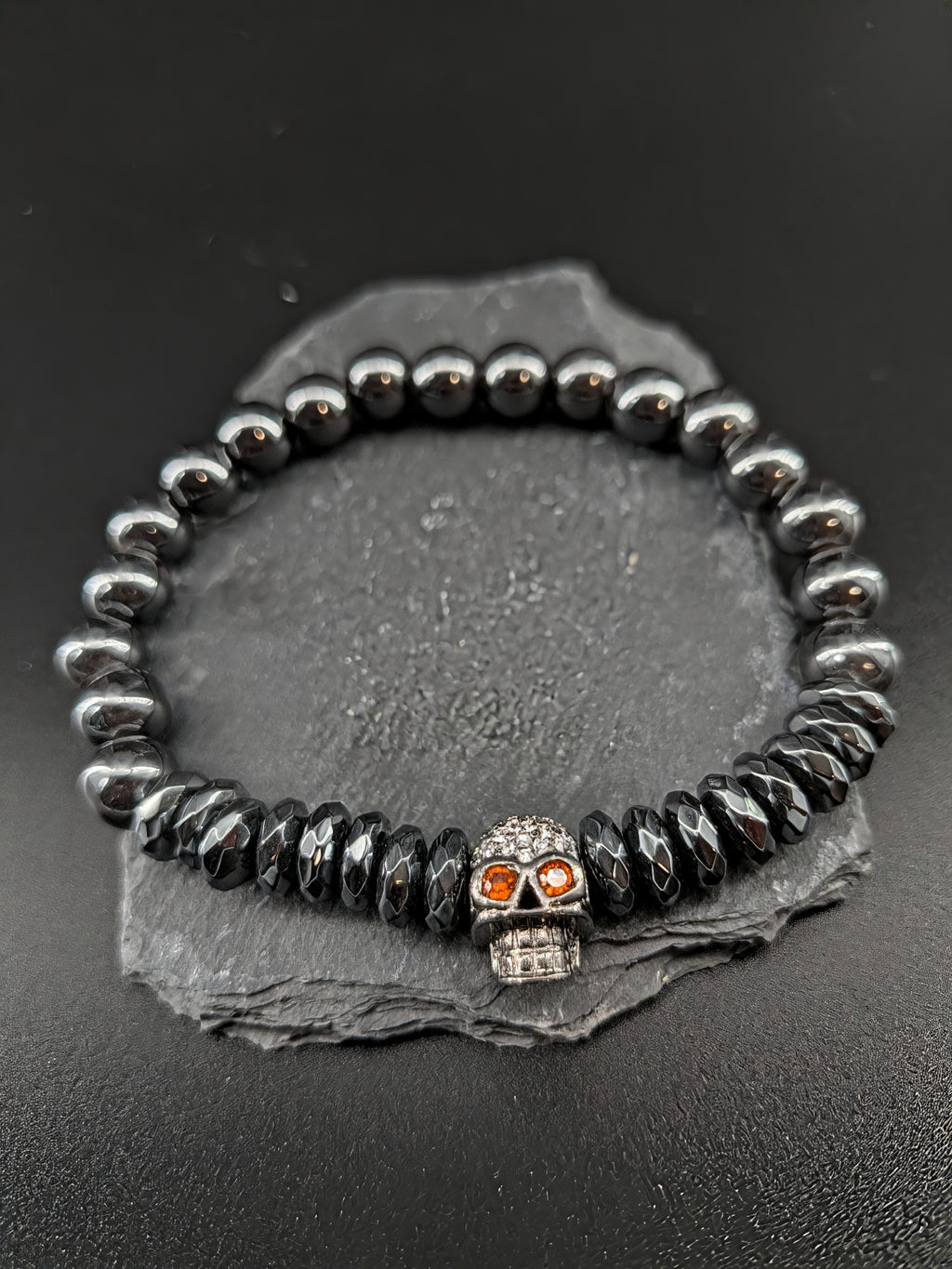 Black beaded bracelet with a skull charm on a dark surface