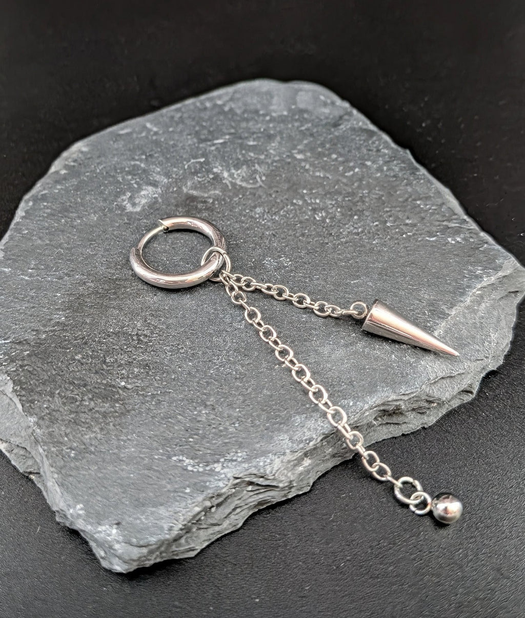 Silver earring with chain and spike on a stone surface