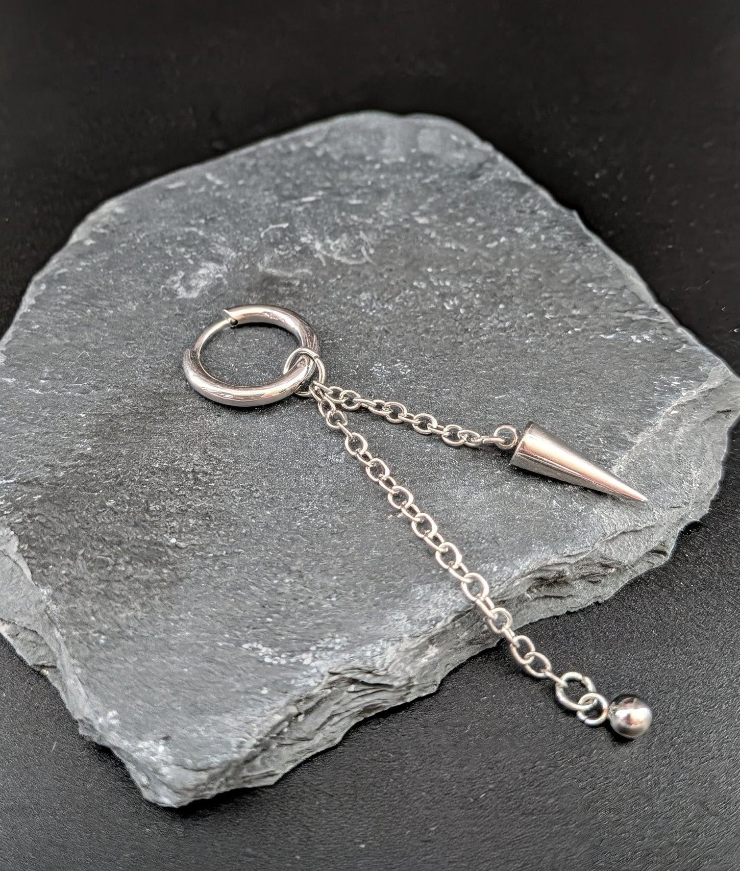 Silver earring with chain and spike on a stone surface