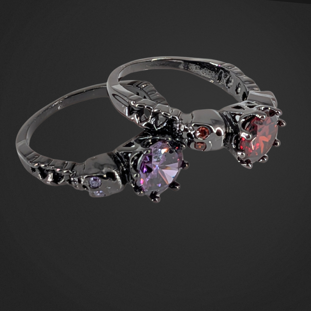Two black gothic rings with gemstones and skulls on a black background