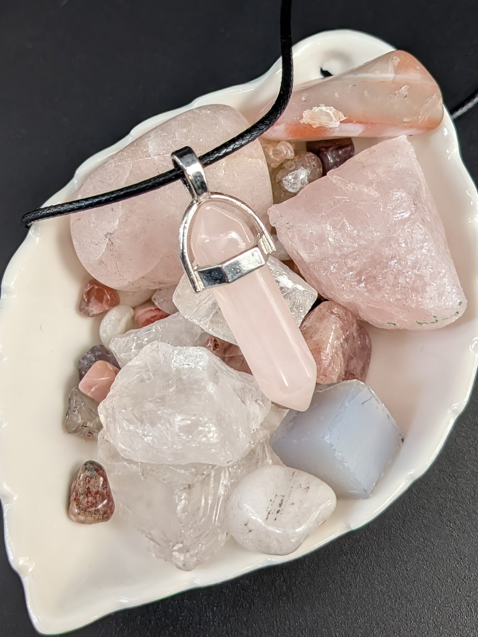 Necklace with a pink crystal pendant on a bed of stones and crystals.