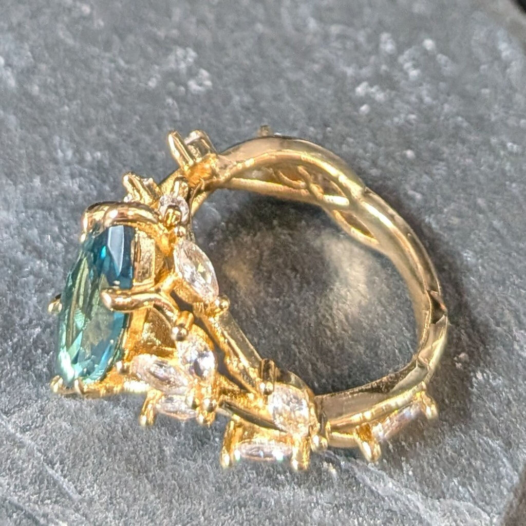 Gold ring with a green gemstone and smaller diamonds on a gray background