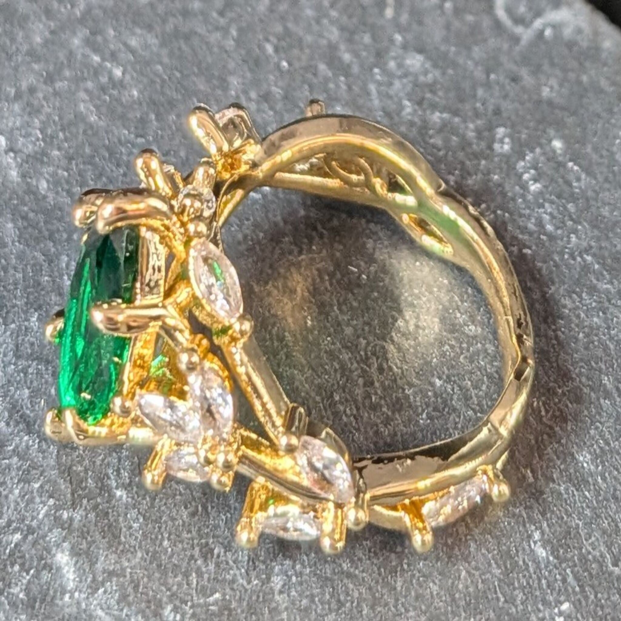 Gold ring with green gemstone and clear stones on a dark background