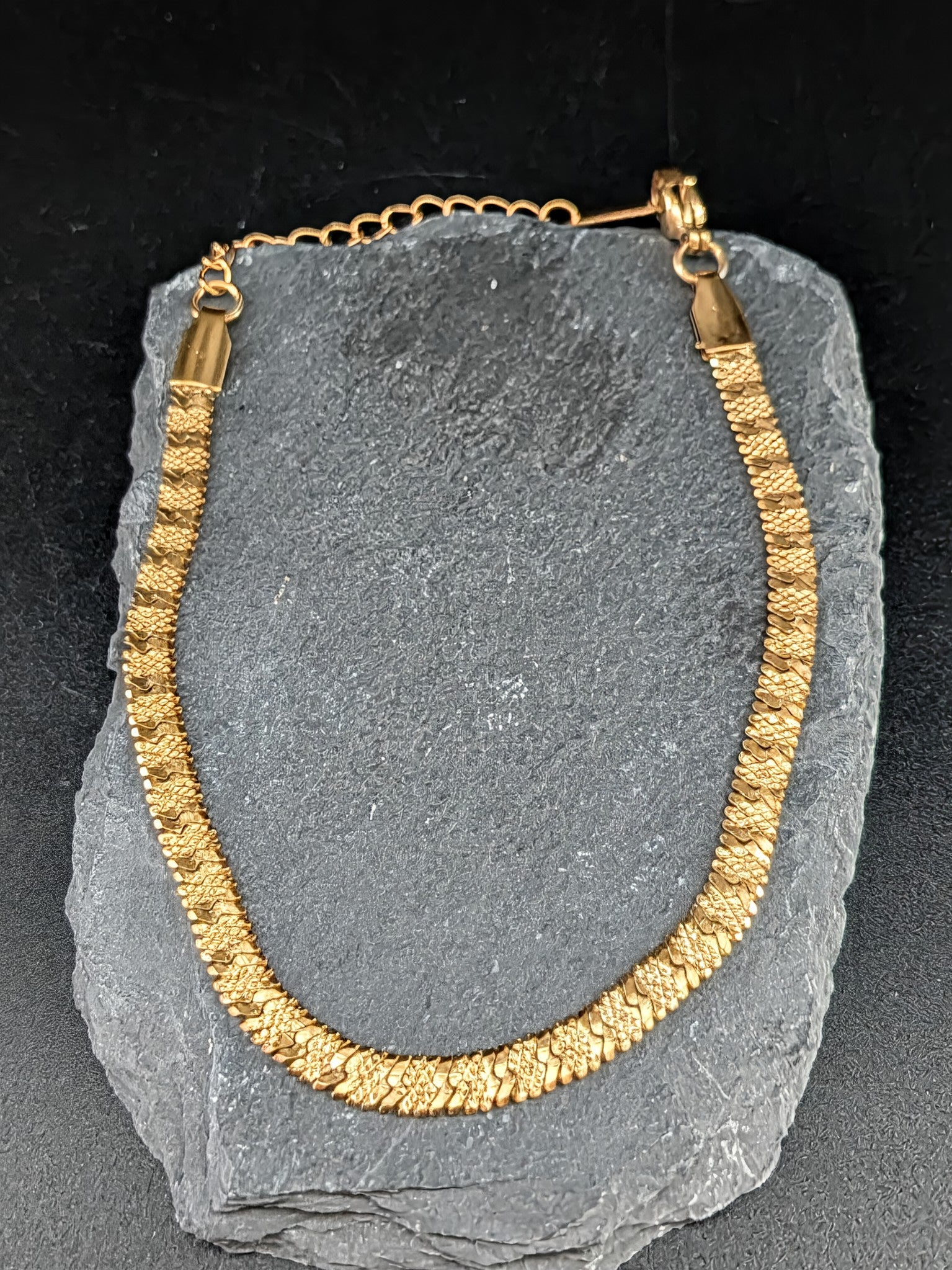 Gold necklace on a gray stone surface with a black background