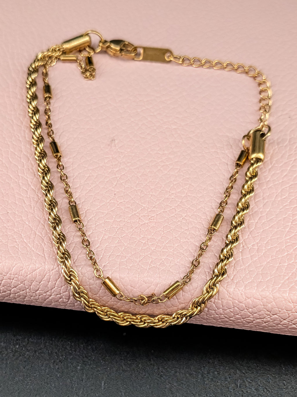 Gold chain bracelet on a pink leather surface