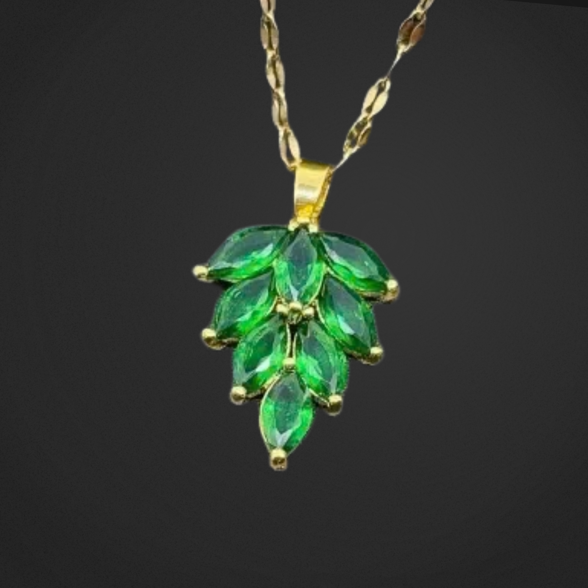 Green leaf-shaped gemstone pendant on a gold chain against a black background